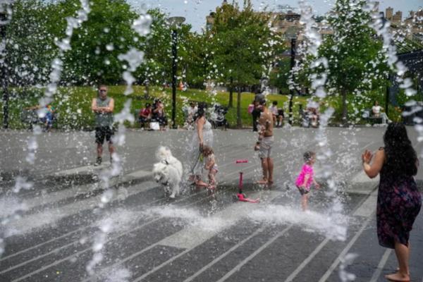 Percikan air tampak membeku menjadi tetesan di sekitar manusia dan seekor anjing Samoyed menikmati istirahat dari panas di bawah fitur air di Georgetown Waterfront Park, Minggu, 23 Juni 2024, di Washington DC. (FOTO: AP PHOTO) 