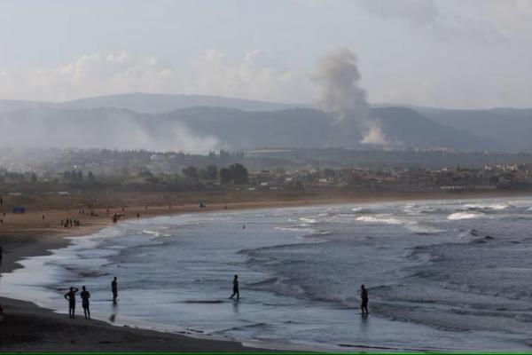 Orang-orang berjalan di pantai saat asap mengepul di sisi perbatasan Lebanon dengan Israel, seperti terlihat dari Tirus, Lebanon selatan 22 September 2024. REUTERS 