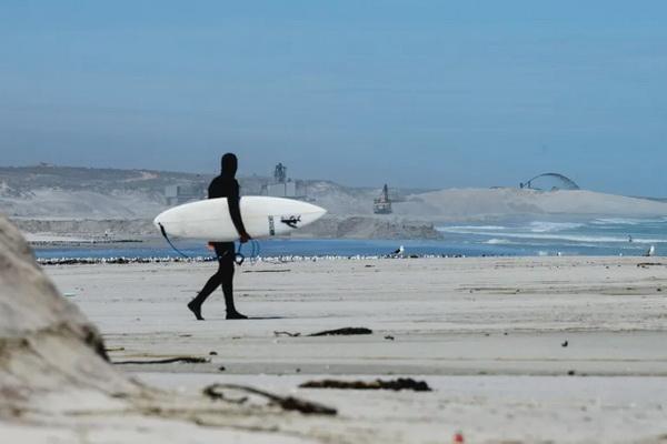 Mike Schlebach berselancar saat Mineral Sands Resources (MSR) milik Australia menggiling pasir pantai untuk mendapatkan mineral berat di Tambang Tormin miliknya. (FOTO: COURTESY OF PROTECT THE WEST COAST) 