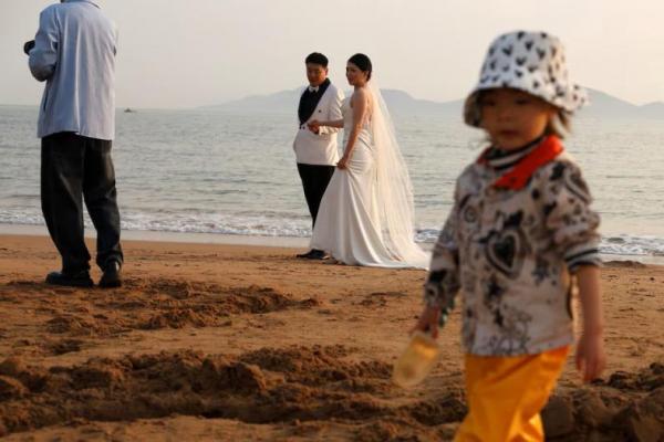 Seorang anak bermain pasir dekat pasangan yang sedang pemotretan pra-pernikahan di sebuah pantai di Qingdao, provinsi Shandong, China, 21 April 2024. REUTERS 