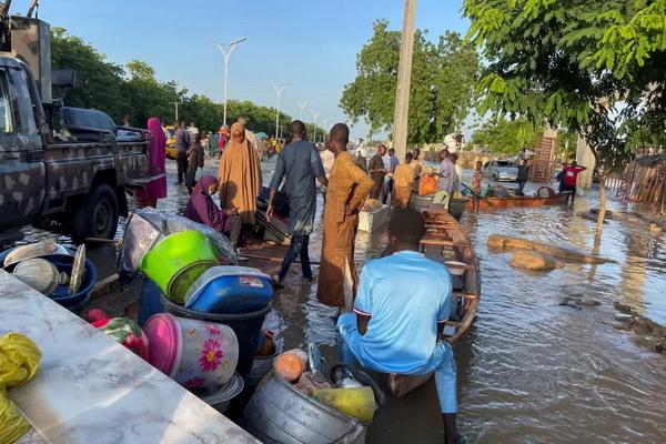 Para korban banjir berdiri di samping barang-barang mereka yang diturunkan dari kano yang membantu mereka menyelamatkan diri di Maiduguri, Nigeria. (FOTO: REUTERS) 