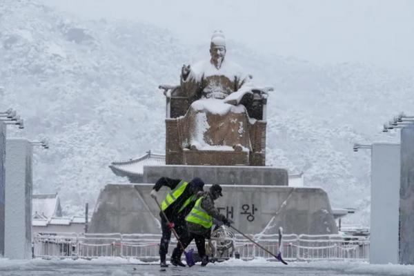 Pekerja membersihkan salju di depan patung Raja Sejong di Lapangan Gwanghwamun di Seoul, Korea Selatan, pada Rabu (27/11/2024). (FOTO: AP PHOTO) 