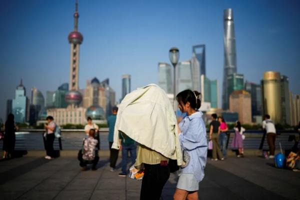 Orang-orang berusaha melindungi diri dari sinar matahari saat berjalan di sepanjang Bund pada hari yang panas, di Shanghai, Tiongkok, pada tahun 2023. (FOTO: REUTERS) 