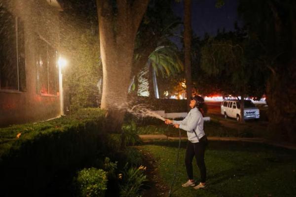 Seorang wanita menyiram area di depan rumahnya sebelum evakuasi akibat kebakaran hutan di lingkungan Pacific Palisades di Los Angeles barat, California, AS, 7 Januari 2025. REUTERS 