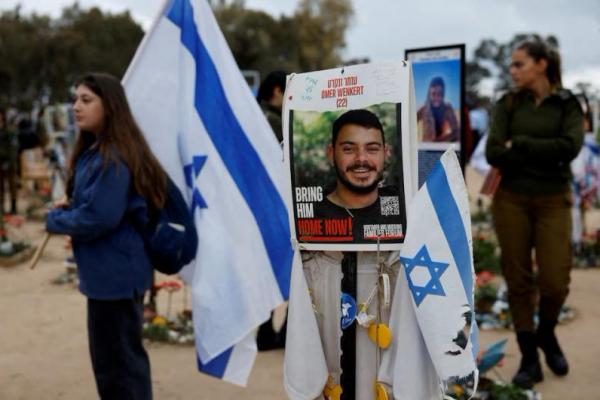 Orang-orang berjalan di dekat poster yang menggambarkan sandera Omer Wenkert, di lokasi festival Nova di Reim, Israel selatan, 19 Februari 2025. REUTERS 